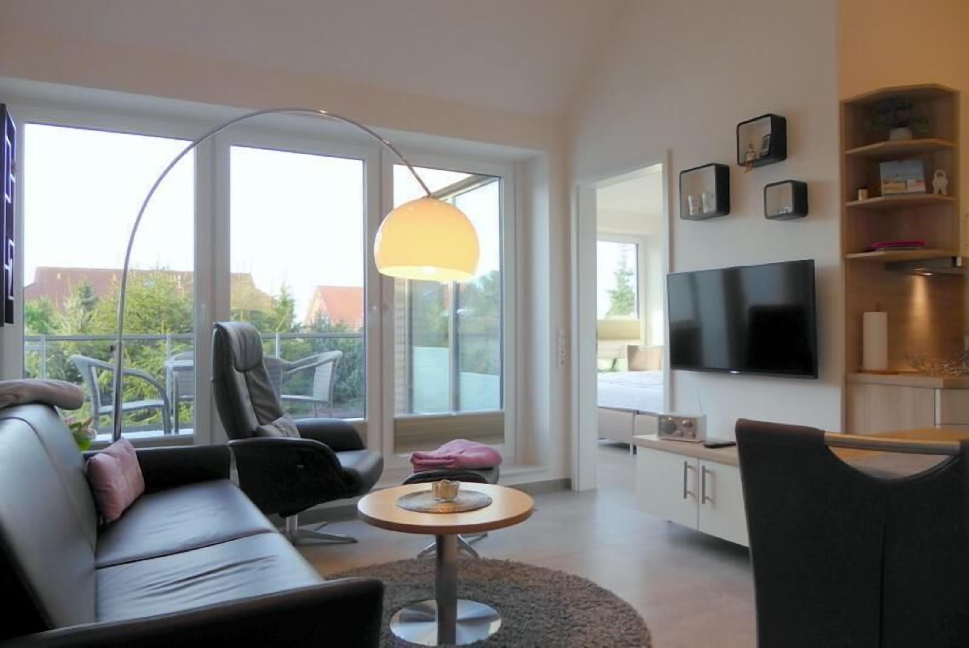 Un salon moderne avec un canapé, une table basse, un téléviseur et une grande fenêtre donnant sur un paysage verdoyant.
