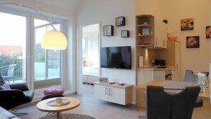 A modern living room with a flat-screen TV, a dining area with a table and chairs, and a sofa.