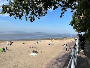 A beach with people sunbathing and walking, a clear sky, and a body of water in the distance.
