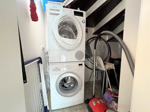 A compact laundry room with two stacked washing machines, a vacuum cleaner, and a hose.