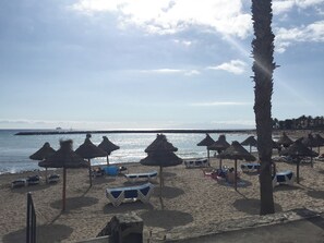 A beach with thatched umbrellas, lounge chairs, and a palm tree. - Castillo Moro—Exclusive Moorish Castle, 10–20 Guests, 11 Bedrooms, Near the Beach (Santa Cruz de Tenerife)