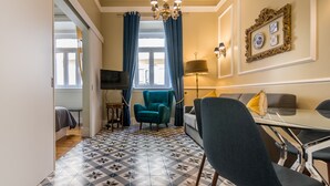Una sala de estar con piso estampado, un sillón azul verdoso, un sofá, una mesa de comedor de vidrio y una araña.