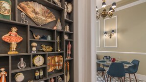 Una habitación con una estantería de madera oscura que exhibe diversos objetos decorativos, un área de comedor con una mesa redonda y sillas, y un candelabro.