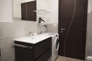 A modern bathroom with a white sink, dark cabinetry, a washing machine, and a towel rack.