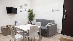 En moderne stue med et hvidt spisebord, en grå sofa og et fladskærms-tv monteret på væggen.