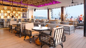 A modern restaurant with a wooden floor, black wicker chairs, and a bar area with stools. - Mercure Samarinda (Samarinda)