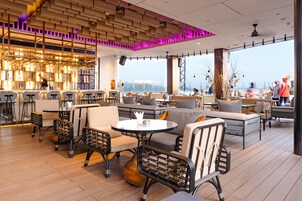Un restaurante moderno con suelo de madera, sillas de mimbre negro y una zona de bar con taburetes.