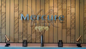 Uma área de recepção de hotel com parede de painéis de madeira, uma grande placa com a inscrição 