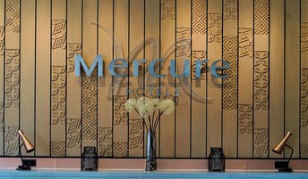 A hotel reception area with a wooden panel wall, a large sign reading "Mercure Hotels", and two black floor lamps.