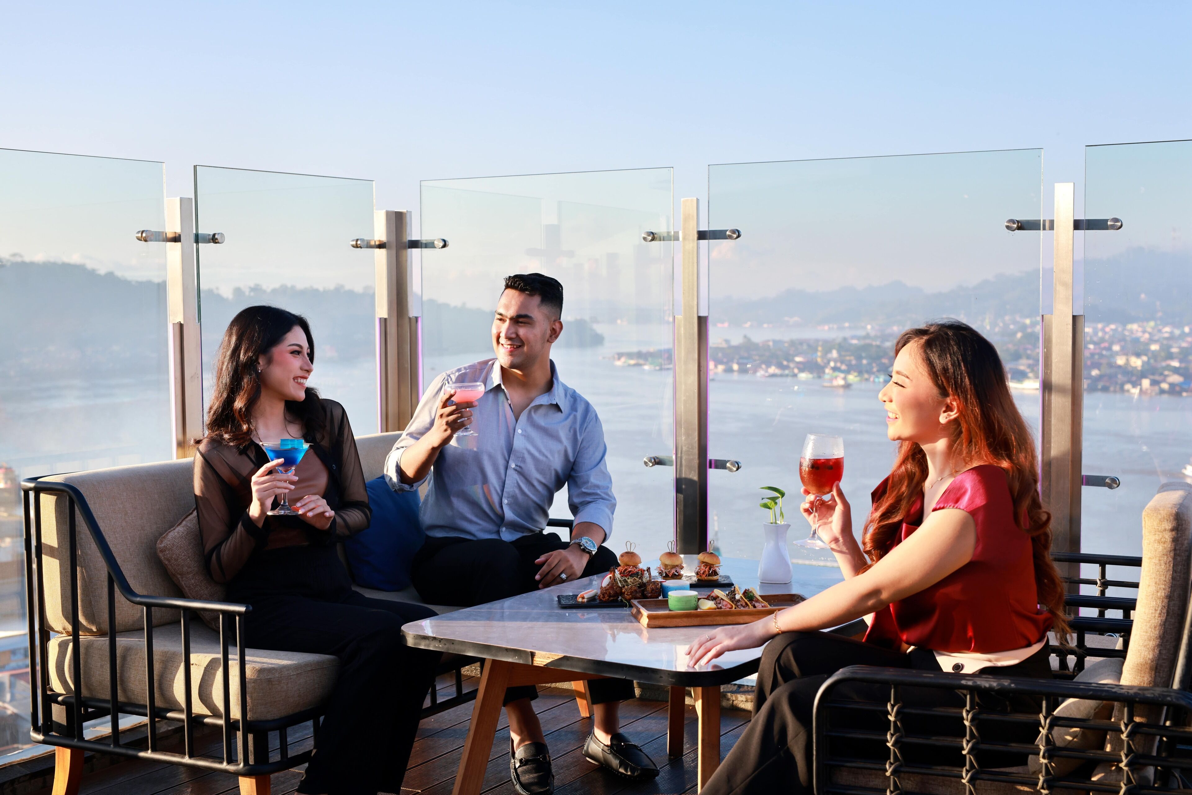 A group of people seated at a table with a city view, enjoying drinks and food.