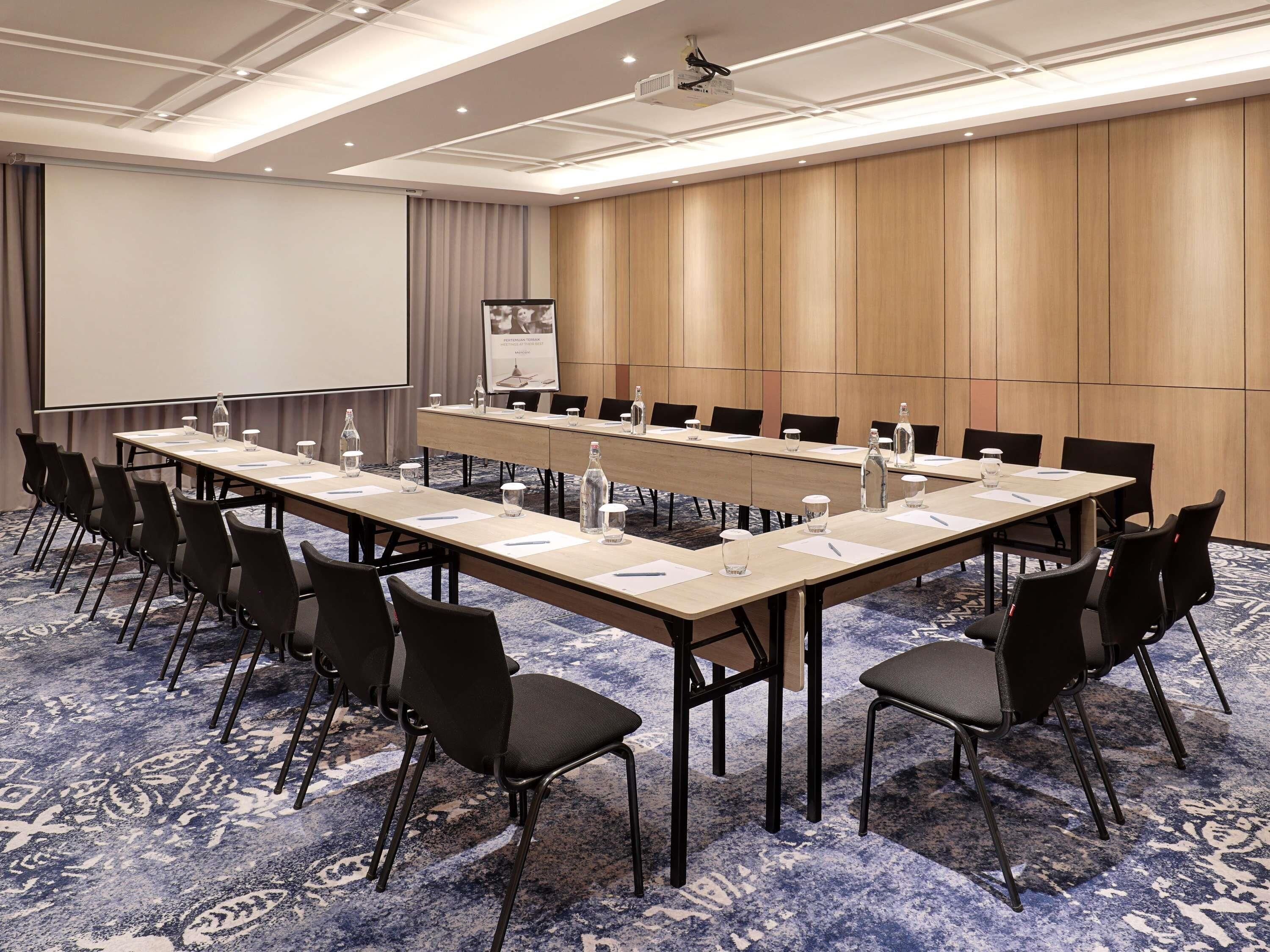 Una sala conferenze con un lungo tavolo, sedie, uno schermo per proiettore e una lavagna per presentazioni.