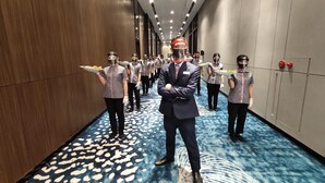 Corredor de hotel com carpete estampado, paredes de madeira e teto moderno com iluminação embutida.