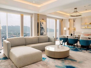 A modern hotel room with a large sofa, a round coffee table, and a dining area with chairs. - Mercure Samarinda (Samarinda)