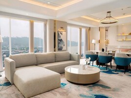 Una habitación de hotel moderna con un sofá grande, una mesa de centro redonda y un comedor con sillas.