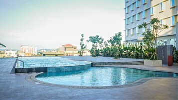 Una piscina en la azotea con borde de azulejos, rodeada por un muro de piedra bajo y plantas en macetas.
