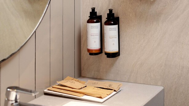 A bathroom with a mirror, two bottles of body lotion and liquid soap, and a tray with towels. - Mercure Samarinda (Samarinda)