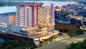 Un hotel moderno con un llamativo letrero 'Mercure Hotel', un vestíbulo espacioso y una vista de la ciudad y el agua al fondo.