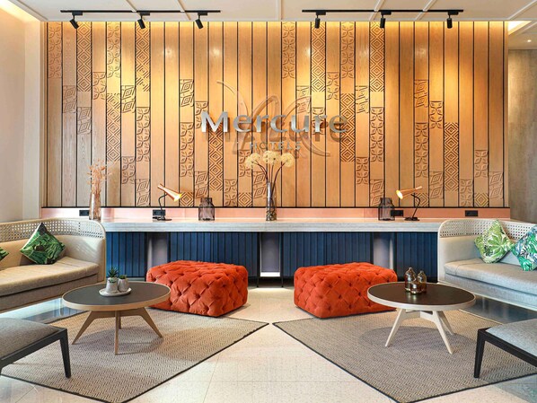 A modern living room with a wooden panel wall, two orange ottomans, a round coffee table, and a sofa with patterned cushions. - Mercure Samarinda (Samarinda)