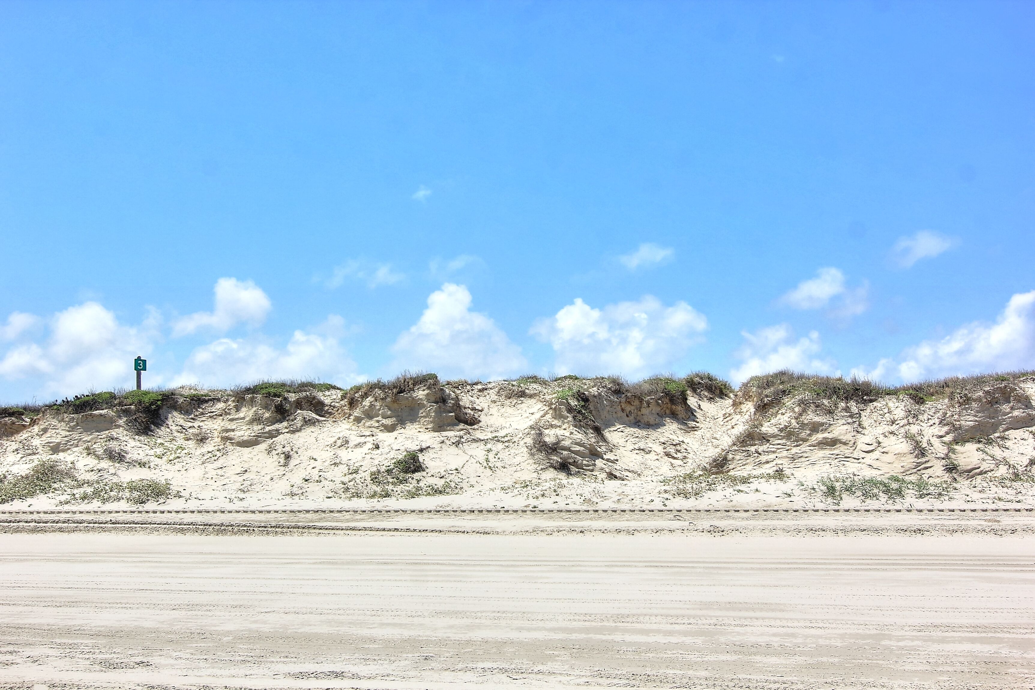 A beach with a road and dunes in the background.