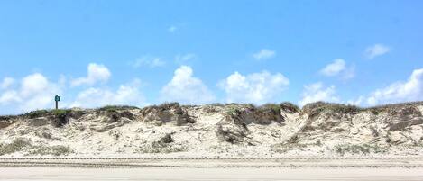 A beach with a road and dunes in the background.