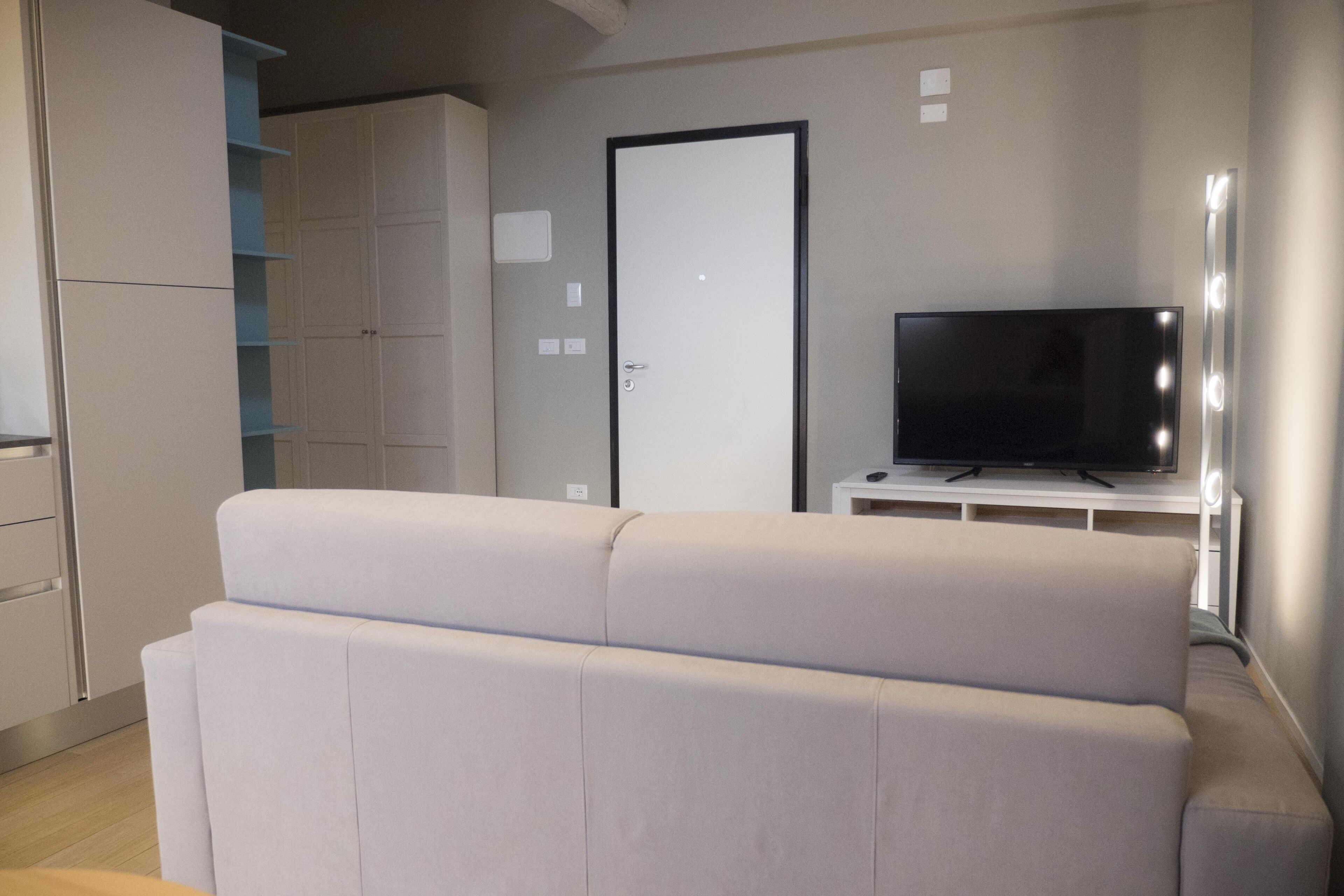 A modern living room with a sofa, a television on a stand, and a wardrobe.