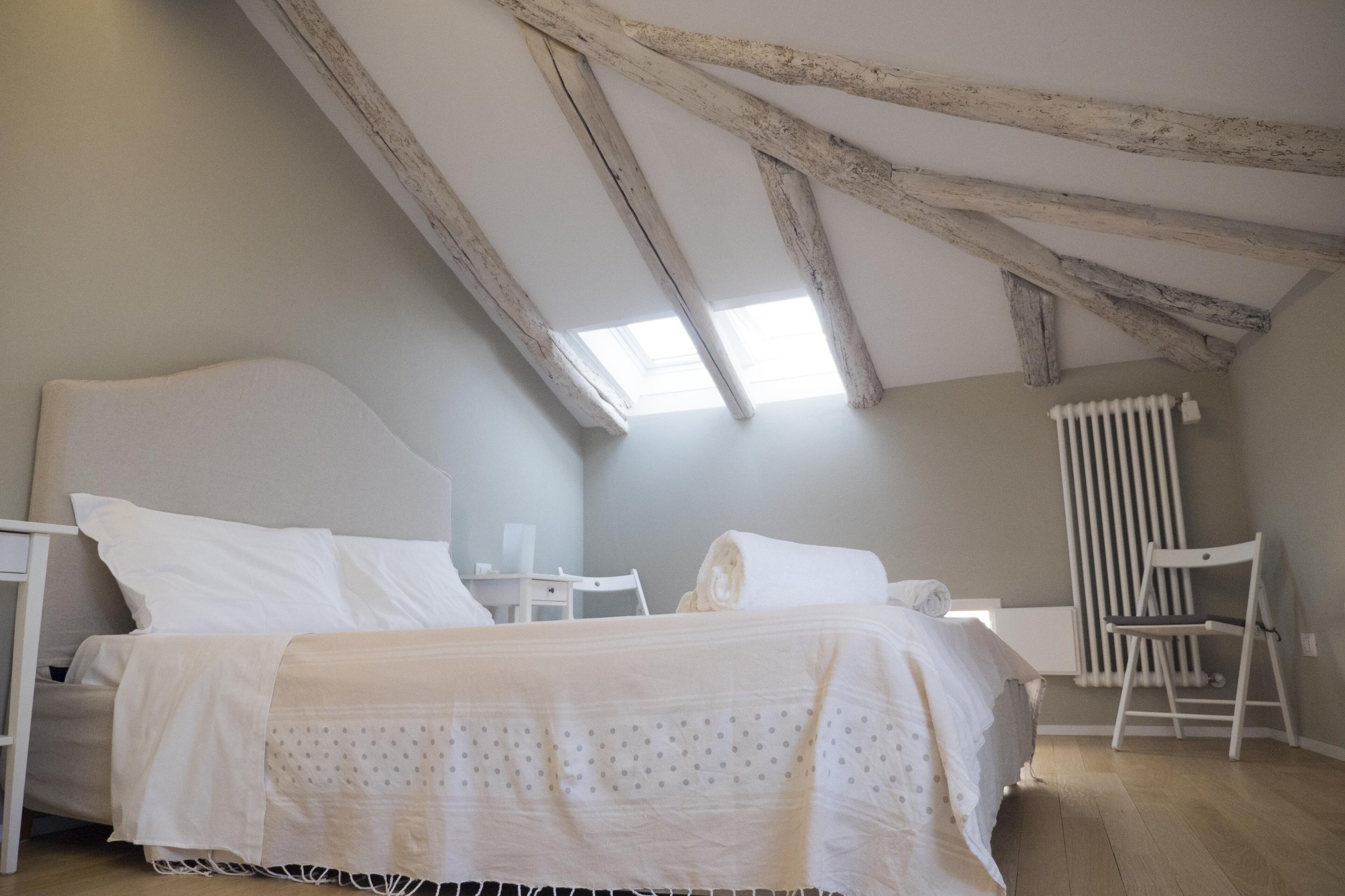 A bedroom with a sloped ceiling, a bed with white bedding, a small table, and a chair.