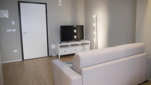 A modern living room with a white sofa, a TV on a white entertainment unit, and a door with a light switch. - Piazza dei Tribunali (Bologna)