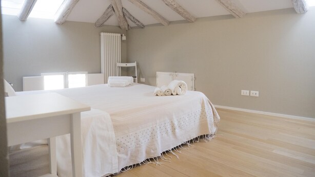 A bedroom with a large bed, a bedside table, a radiator, and a window. - Piazza dei Tribunali (Bologna)