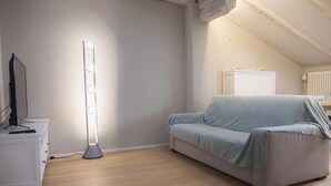 A room with a white dresser, a standing lamp, a light blue sofa, and a white radiator. - Piazza dei Tribunali (Bologna)