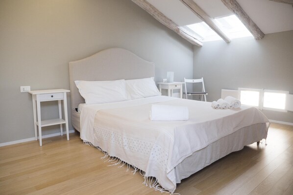 A bedroom with a large bed, two bedside tables, a chair, and a skylight. - Piazza dei Tribunali (Bologna)