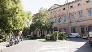 A street view with parked motorcycles, a white van, and a building with the sign "PALAZZO DI GIVIZZIA." - Piazza dei Tribunali (Bologna)