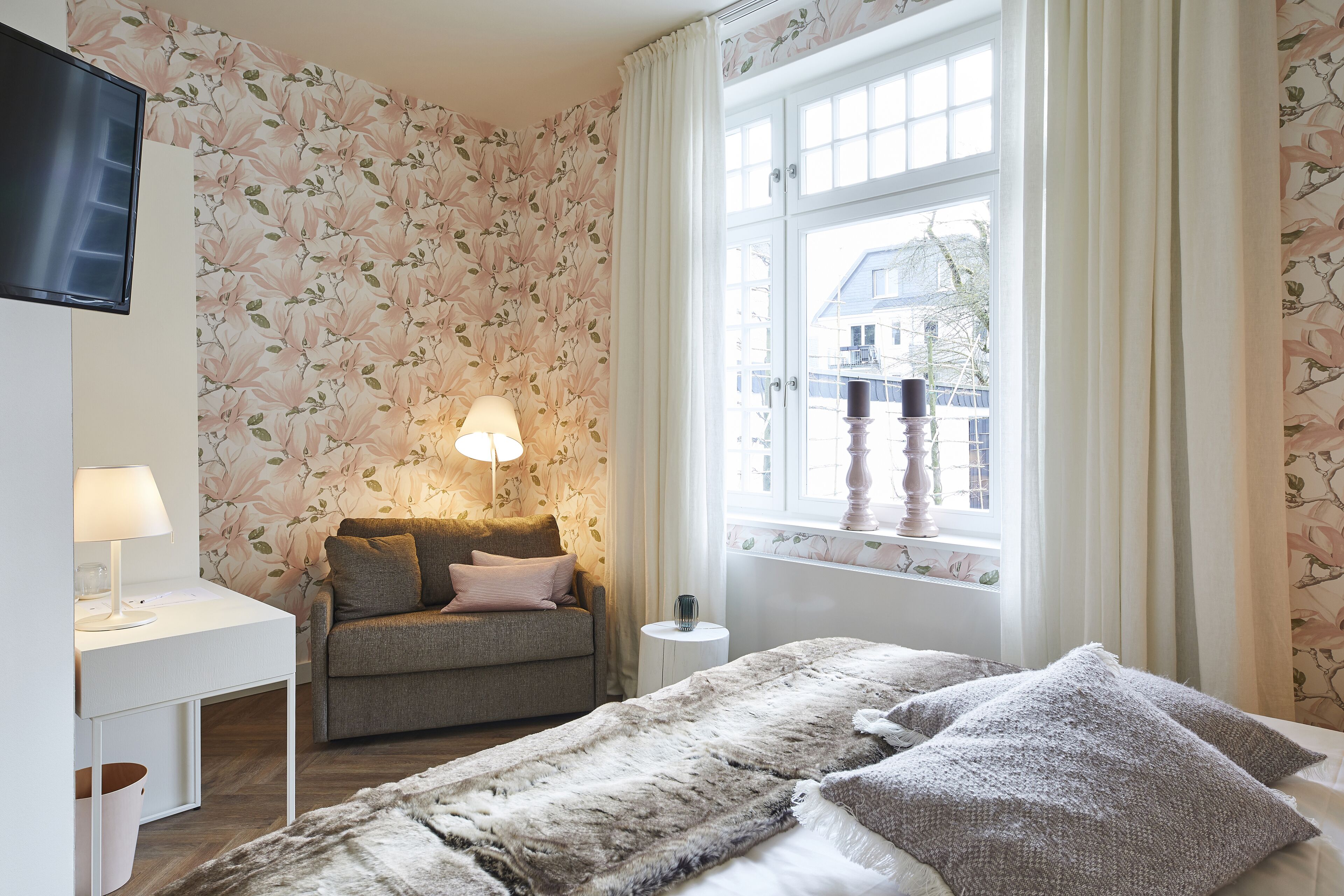 Une chambre à coucher avec un lit, un canapé, une télévision, une lampe et une fenêtre avec des rideaux.