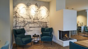 A modern living room with a fireplace, two green armchairs, a coffee table, and a large wall mural. - BUITERLING Hotel (Brilon)