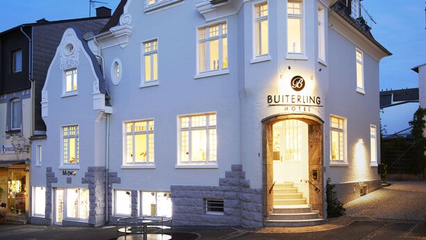 A historic building with a prominent tower, a sign for 'BUITERLING HOTEL', and a circular outdoor seating area. - BUITERLING Hotel (Brilon)