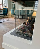 Una sala de estar moderna con chimenea de vidrio, suelo de madera y sillones color turquesa.