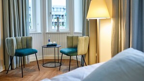 A hotel room with two armchairs, a small round table with a bottle and glasses, a lamp, and a bed with white bedding. - BUITERLING Hotel (Brilon)
