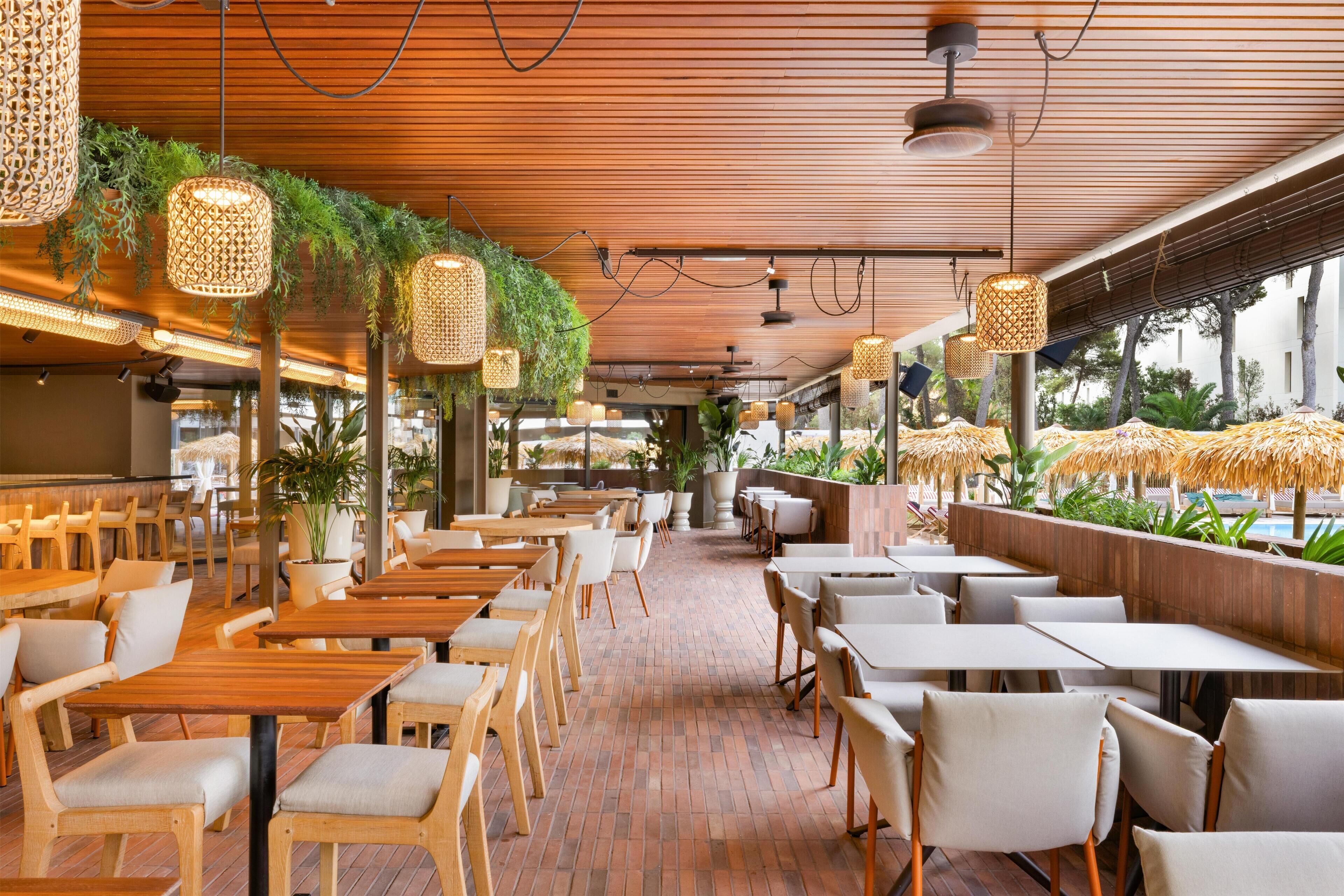 Un ristorante con tavoli e sedie di legno, piante pensili e pavimento in mattoni.