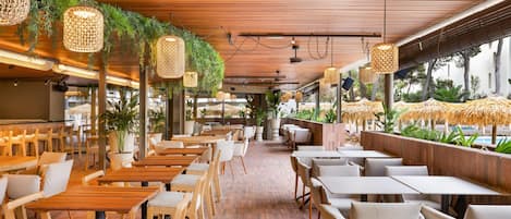 Un restaurante con mesas y sillas de madera, plantas colgantes y piso de ladrillo.