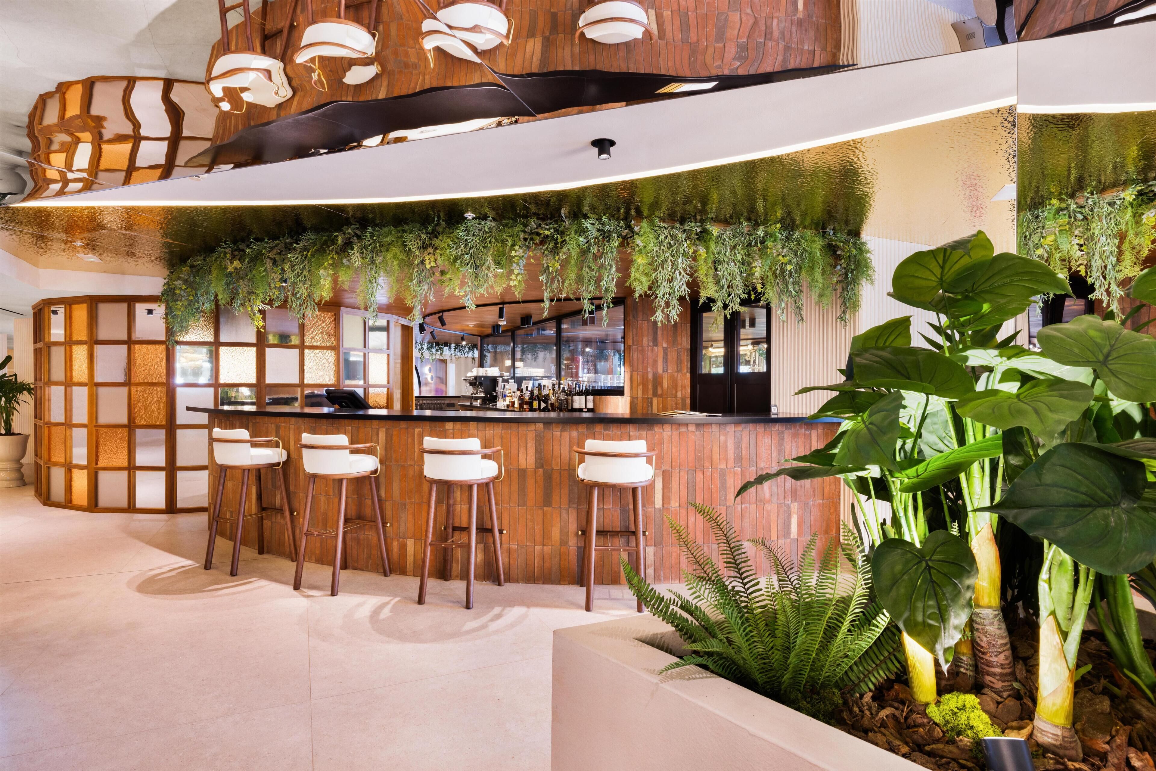A modern bar area with wooden accents, bar stools, and lush greenery.