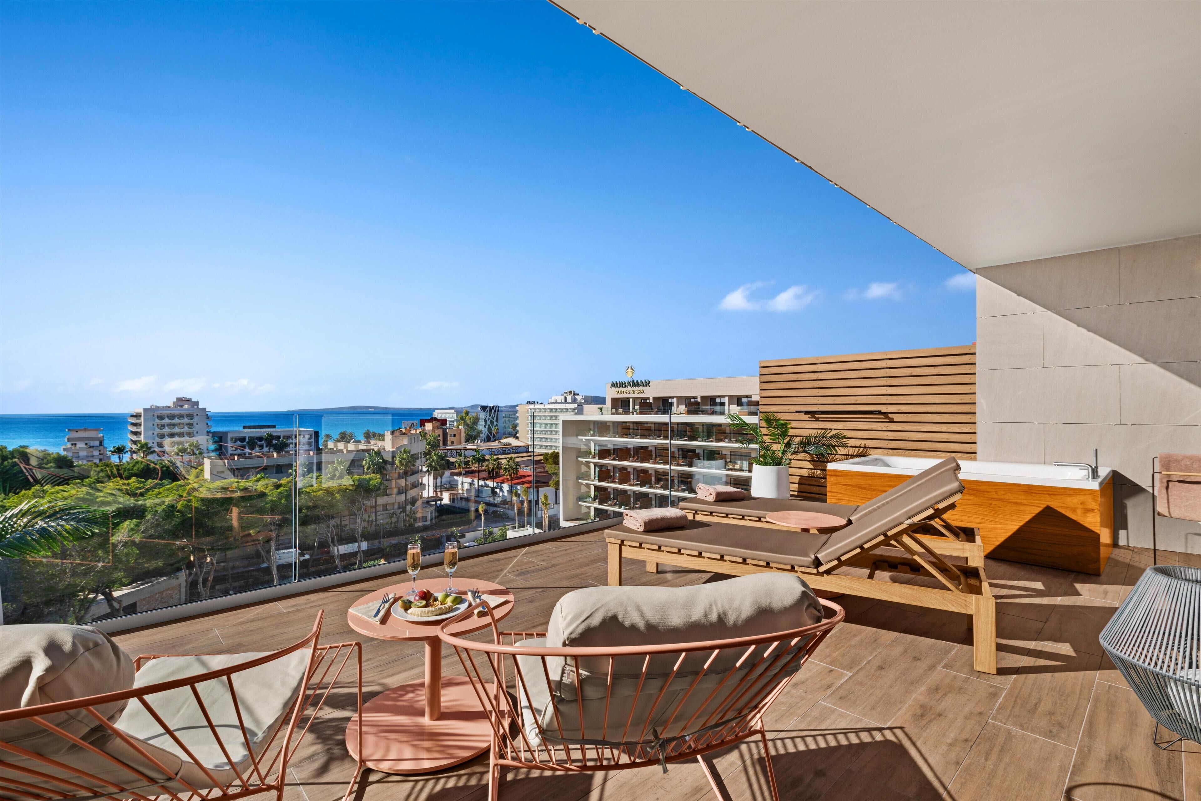 Un balcone con vista sul mare e sulla città, arredato con sedie, un tavolo e una panca di legno con una vasca.