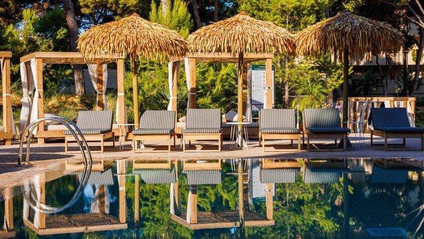 A pool area with wooden loungers and thatched umbrellas, surrounded by greenery. - Aubamar Palma Resort (Palma de Mallorca)
