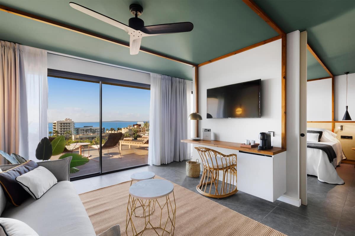 Una habitación de hotel moderna con un balcón grande, televisor de pantalla plana, zona de comedor y sofá.