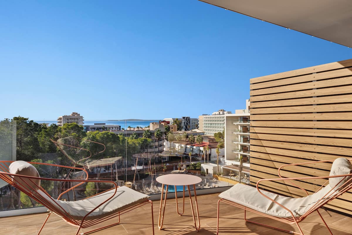 Un balcón con dos sillones de descanso, una mesita redonda y vistas al mar y edificios.