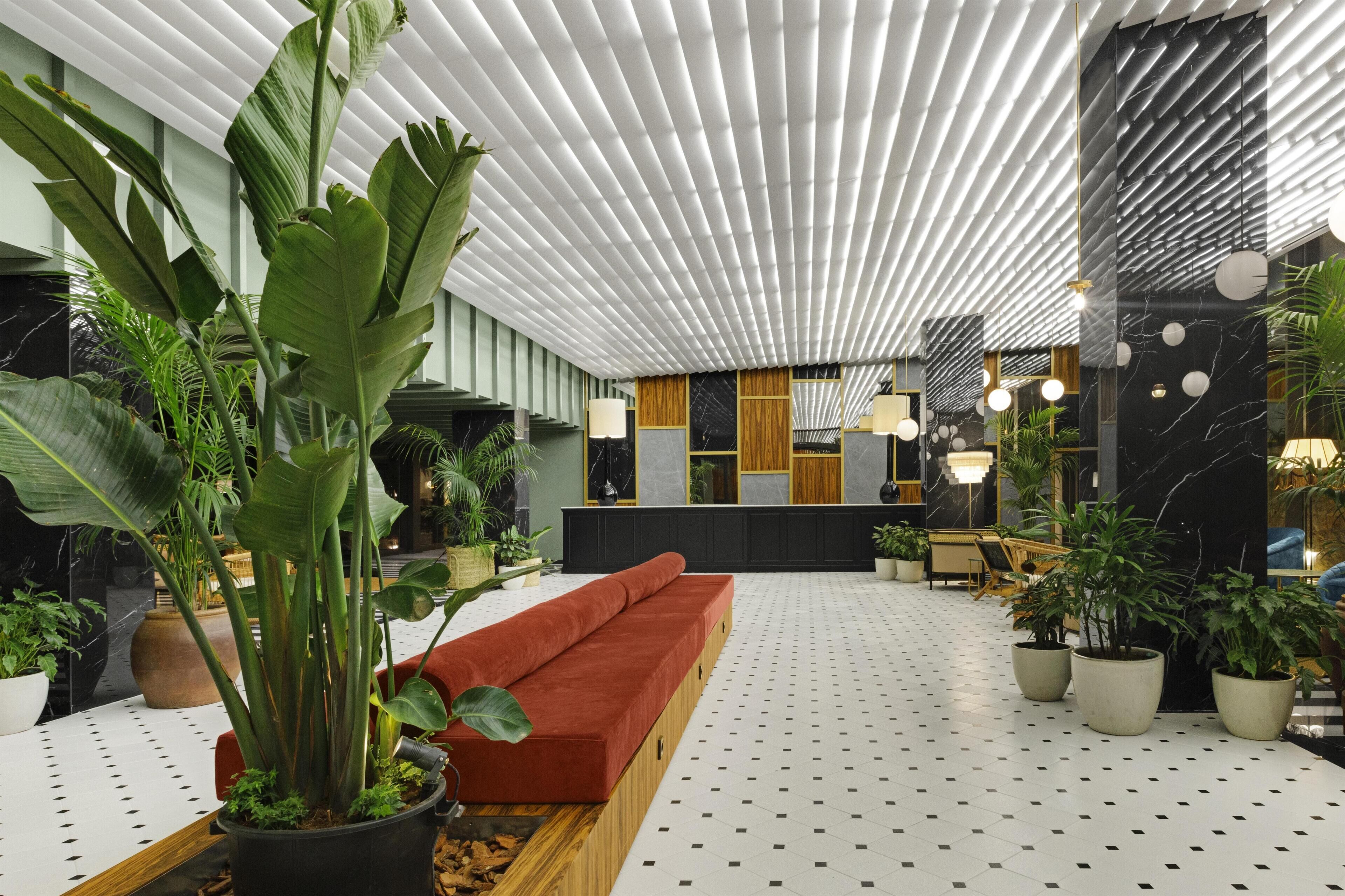 Un lobby moderno con un sofá rojo, plantas en macetas y un suelo estampado.