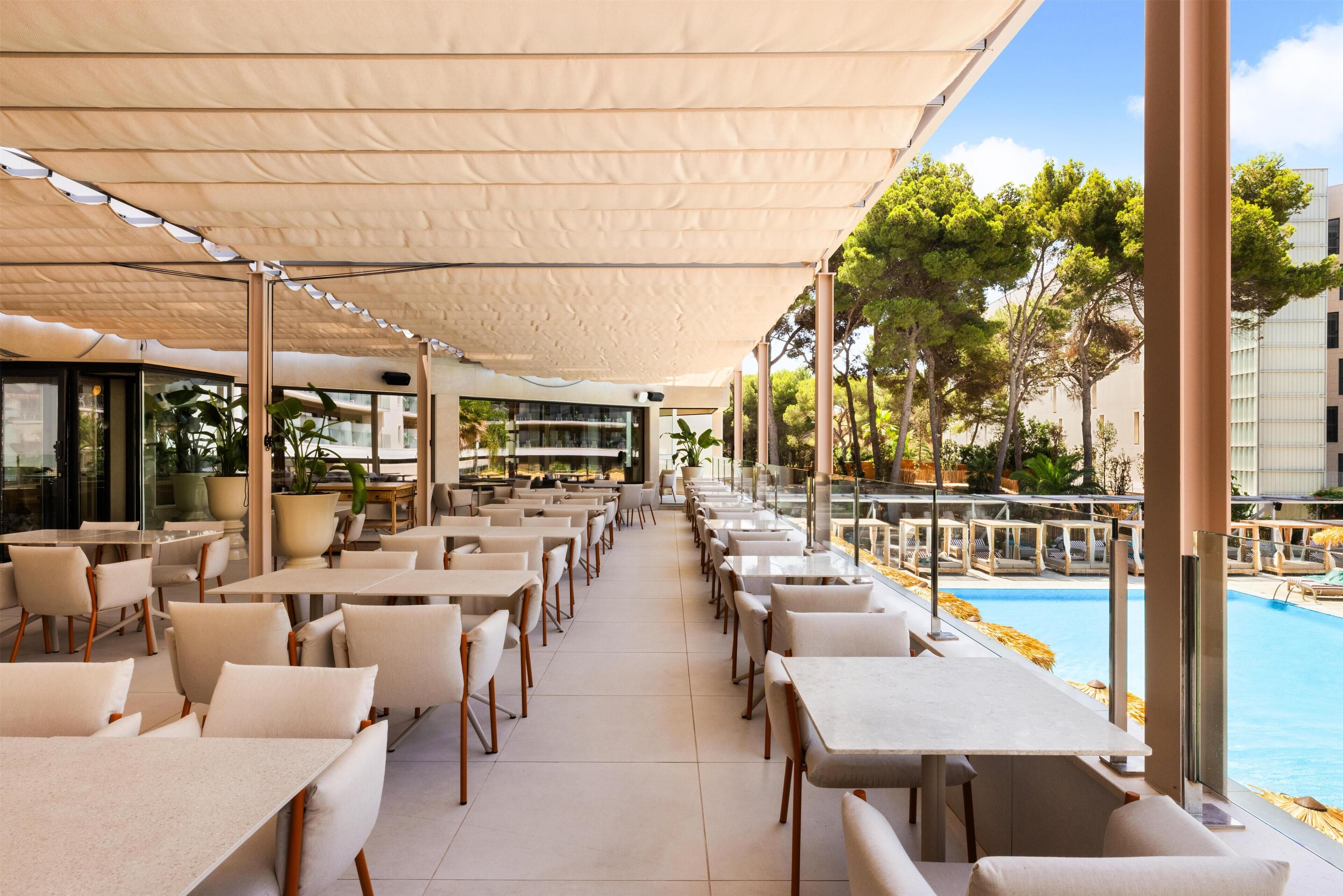 A covered outdoor seating area with tables and chairs, overlooking a swimming pool.