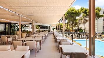 A covered outdoor seating area with tables and chairs, overlooking a swimming pool.