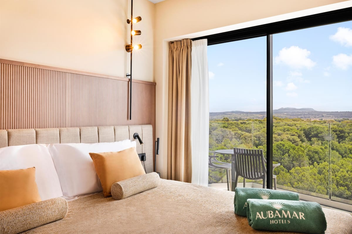 Habitación de hotel con una cama grande, vistas del paisaje y un balcón con mesa y silla.