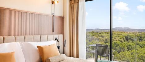 A hotel room with a large bed, a view of the landscape, and a balcony with a table and chair.