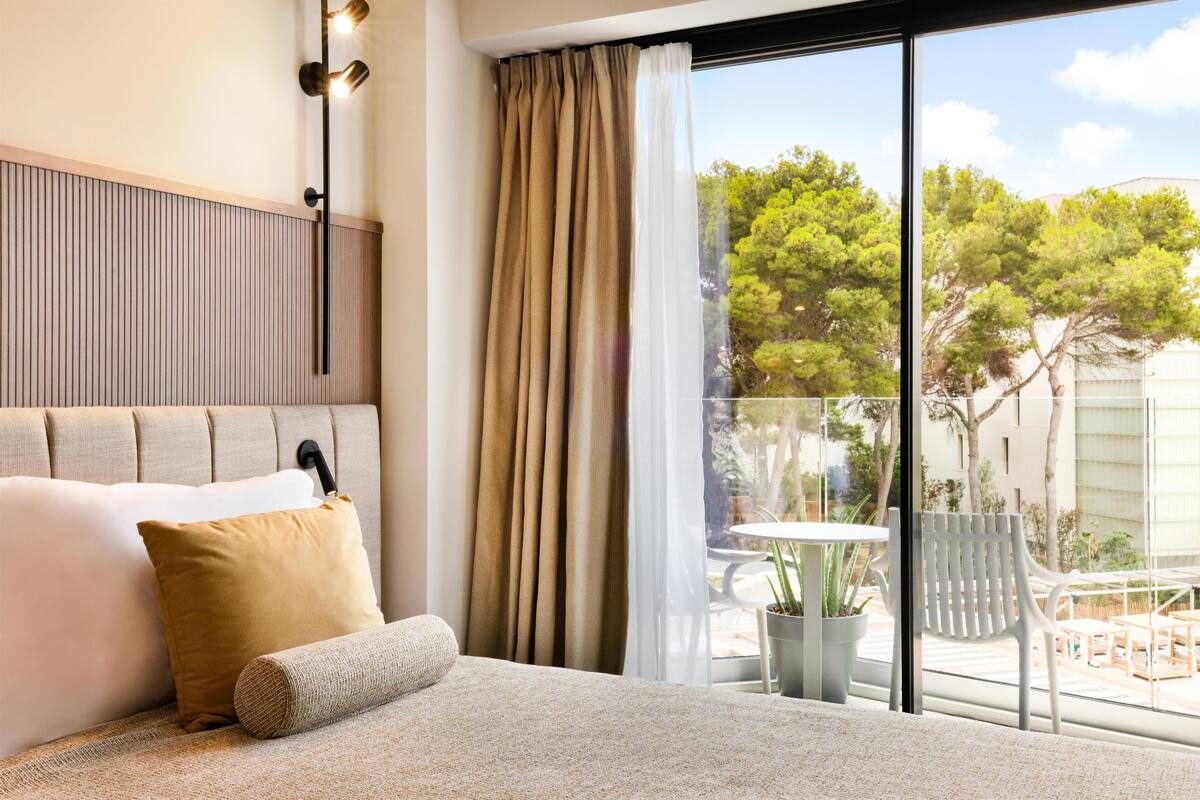 Un dormitorio con una cama grande, cabecera, ventana con cortinas y vistas al exterior.