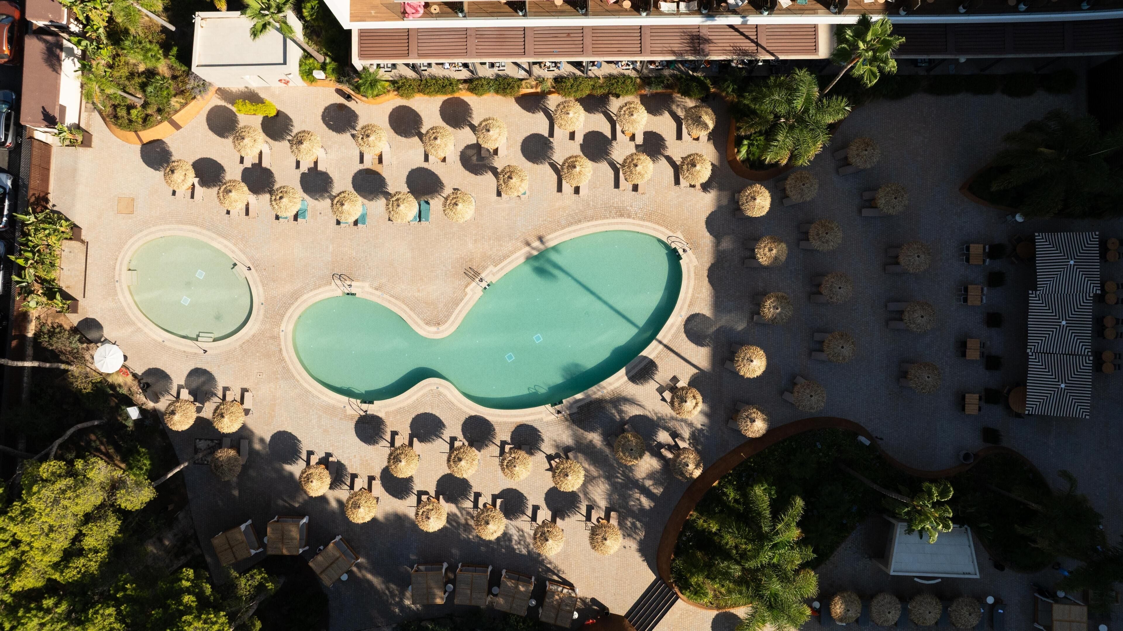 Luchtbeeld van een resort met twee zwembaden, ligbedden en een overdekte zithoek.